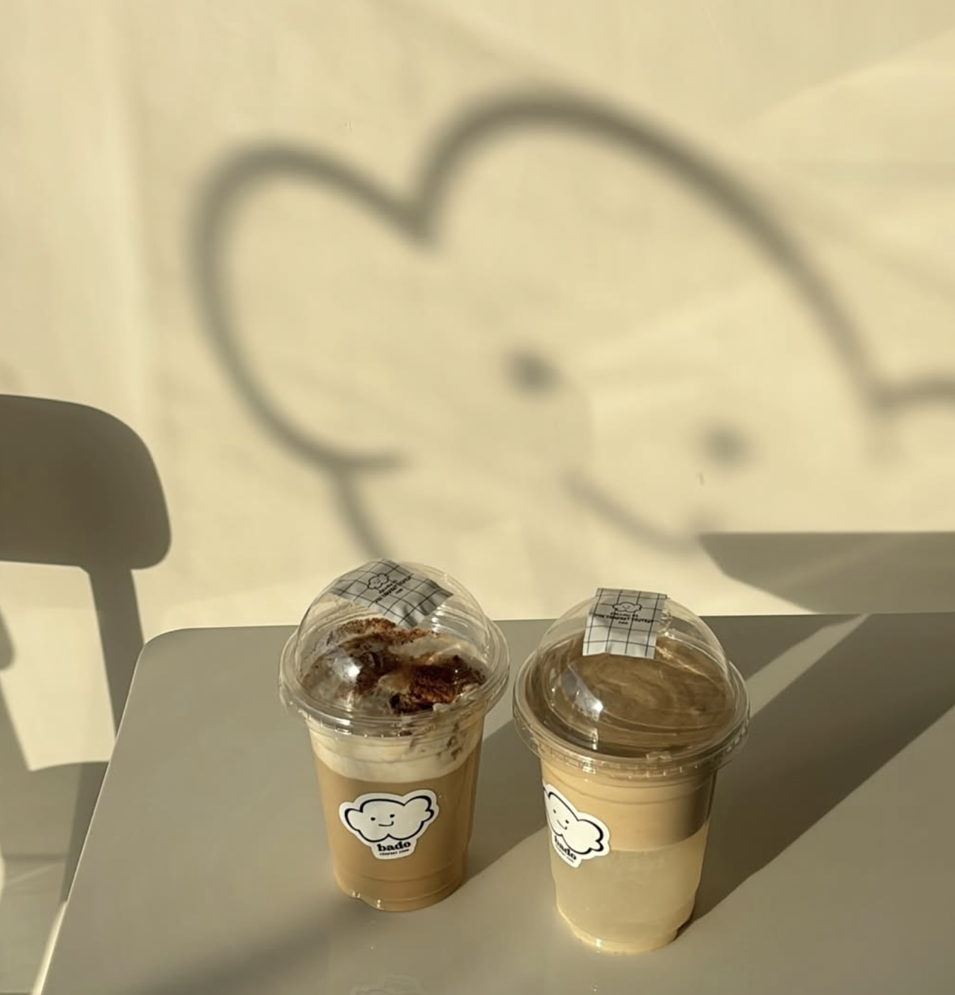 Two Bado iced coffees on a café table with the cloud mascot shadow on the wall
